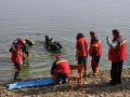 Potápači prinášajú telo rybára ku brehu.